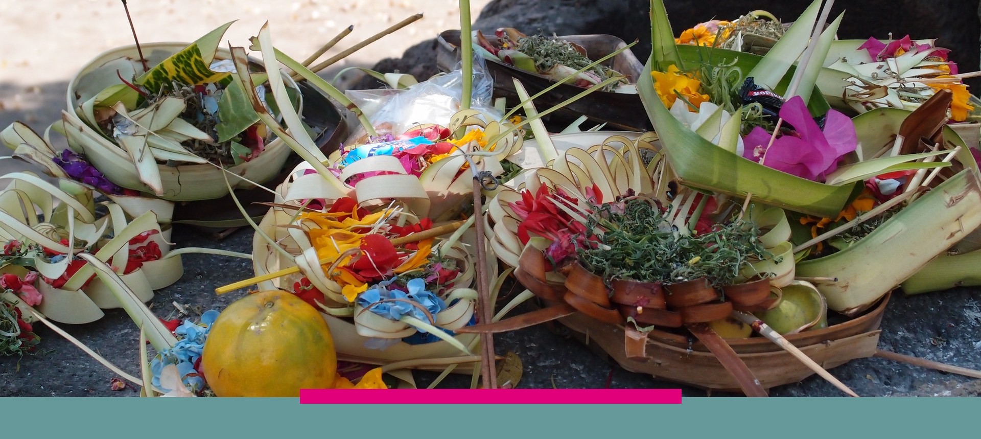 Balinesische Opferschalen aus Palmblättern mit bunten Blüten auf einem Stein